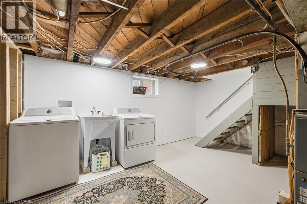 Basement utility area featuring a laundry sink, exposed wood ceiling joists, white walls, and concrete flooring - 81 Vale Avenue, St. Catharines, ON