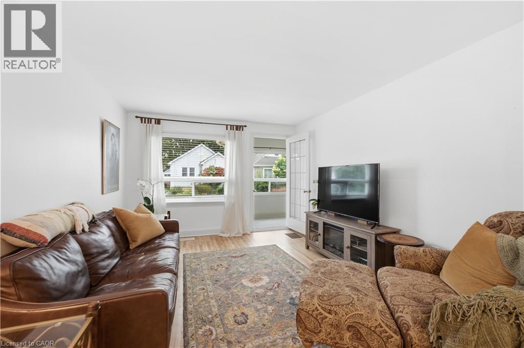 Living area featuring light wood-finish flooring, white walls, and a large window with white blinds - 81 Vale Avenue, St. Catharines, ON