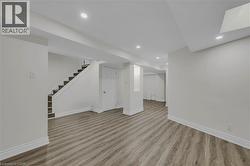 Spacious room featuring wood-finish flooring, recessed lighting, white trim, light-toned walls, and a staircase with dark treads -