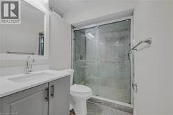 Contemporary bathroom featuring a glass-enclosed shower with stone-finish tile, a light gray vanity with a built-in sink, a wall-mounted mirror, and tile flooring -