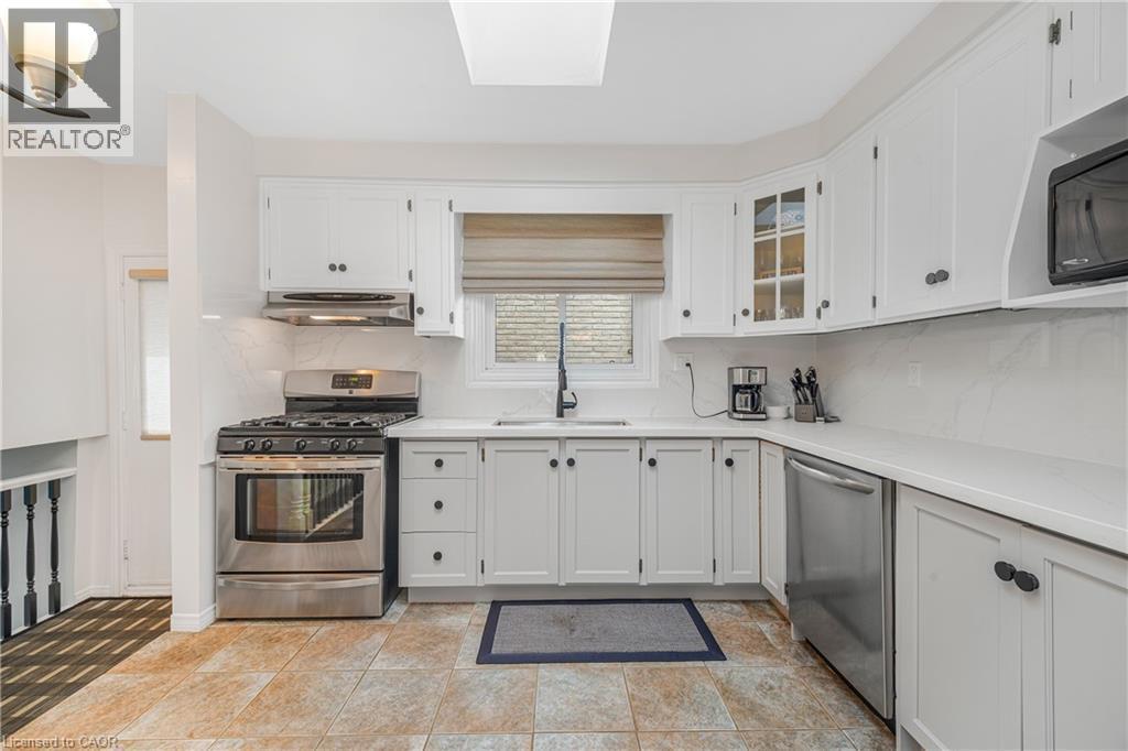 Bright kitchen featuring white cabinetry, stainless steel appliances, a tile backsplash, and light countertops - 23 Millpond Place, Mountain, ON
