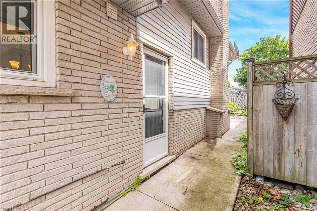 Exterior side entrance featuring light brick siding, white vinyl siding, a side door, and a concrete pathway - 23 Millpond Place, Mountain, ON