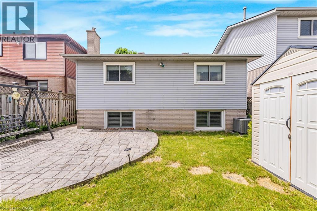 Rear exterior featuring light grey siding with white trim windows, a brick foundation, and a central chimney - 23 Millpond Place, Mountain, ON