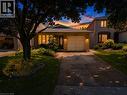 Brick facade residence featuring an attached garage with carriage-style door, a paved driveway, and established front yard landscaping - 23 Millpond Place, Hamilton, ON 
