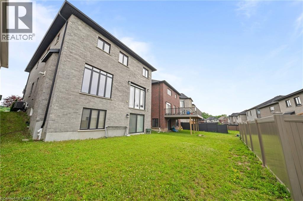 Spacious backyard featuring a sloped lawn and a grey brick exterior - 130 Pondcliffe Drive, Kitchener, ON