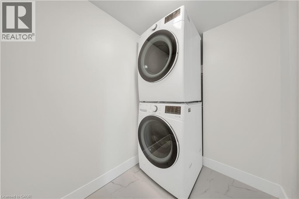 Dedicated laundry area featuring a stacked washer and dryer, contemporary white baseboards, and light-toned tile flooring - 3085 Kingsway Drive Unit# 21, Kitchener, ON
