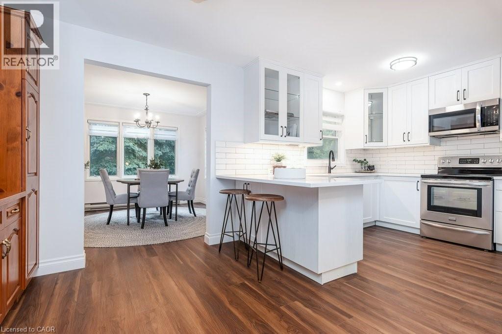 Bright kitchen featuring white cabinetry, subway tile backsplash, stainless steel appliances, and wood-finish flooring - 139 Mackay Crescent, Waterloo, ON