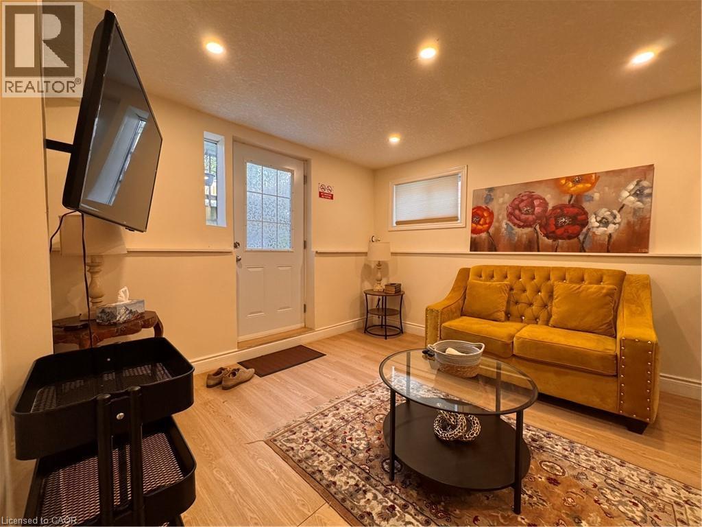 Living area featuring wood-finish flooring, recessed ceiling lighting, a white panel door with frosted glass, and a window with a roller shade - 110 Marl Meadow Drive Unit# B, Kitchener, ON