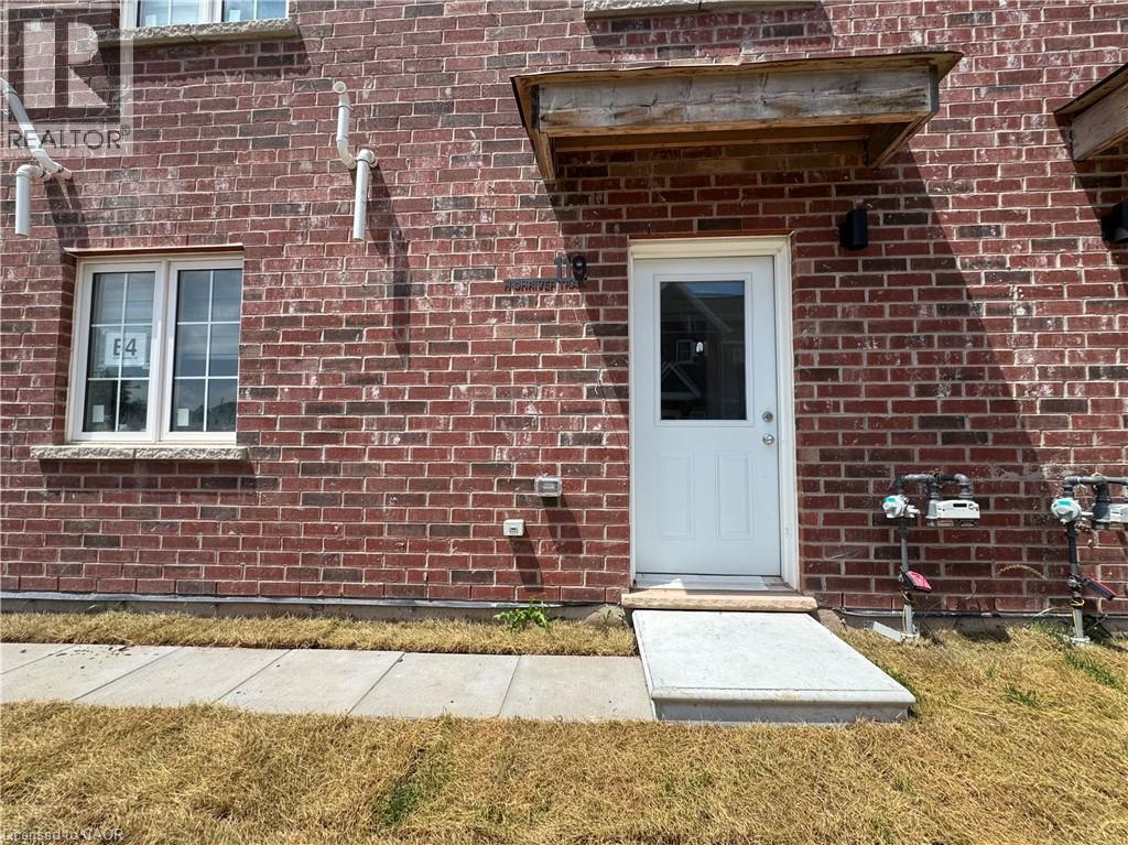 Red brick exterior featuring a white paneled door, a single-hung window with white framing, and a concrete pathway leading to the entrance - 119 Highriver Trail Unit# Main, Welland, ON - Outdoor