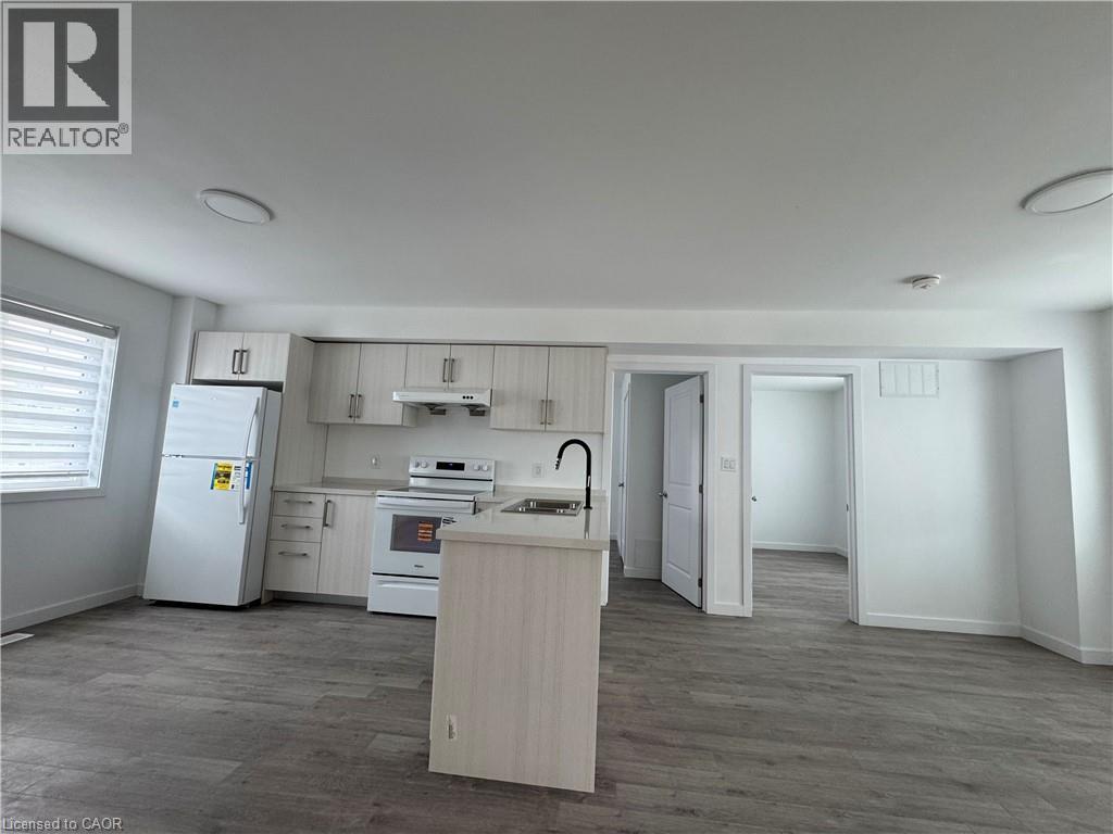 Open-concept kitchen featuring light-toned cabinetry, a central island with an integrated sink and gooseneck faucet, white appliances, and wood-finish flooring - 119 Highriver Trail Unit# Main, Welland, ON - Indoor Photo Showing Kitchen
