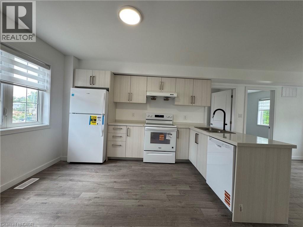 Kitchen featuring wood-finish cabinetry, white appliances, a center island with sink and integrated dishwasher, and wood-finish flooring - 119 Highriver Trail Unit# Main, Welland, ON - Indoor Photo Showing Kitchen With Double Sink