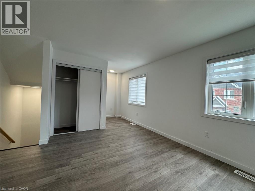 Spacious room with wood-finish flooring, two windows with blinds, a built-in closet with sliding doors, and a staircase with a wood handrail - 119 Highriver Trail Unit# Main, Welland, ON - Indoor Photo Showing Other Room