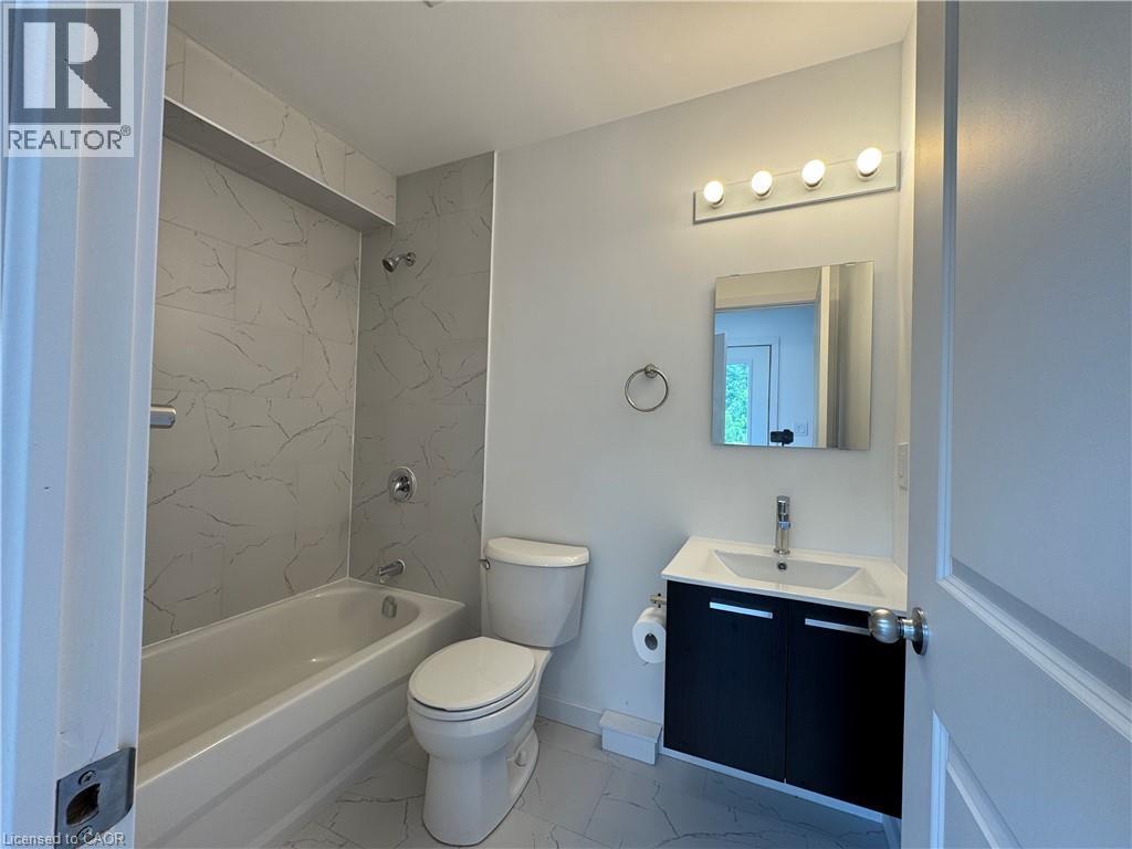 Bathroom featuring a white bathtub with chrome fixtures, a toilet, and a vanity with a white basin sink and dark cabinetry - 119 Highriver Trail Unit# Main, Welland, ON - Indoor Photo Showing Bathroom