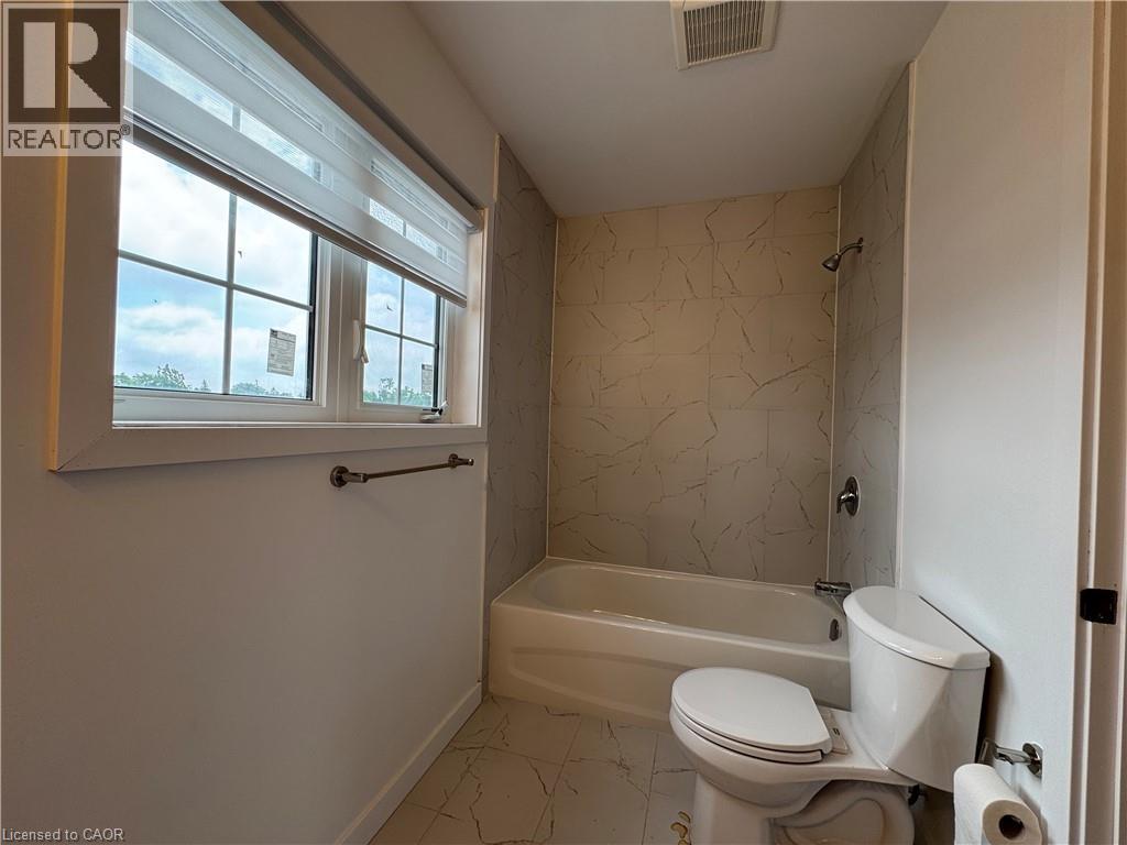 Full bathroom featuring a window with privacy blinds, a white toilet, and a bathtub with a shower - 119 Highriver Trail Unit# Main, Welland, ON - Indoor Photo Showing Bathroom