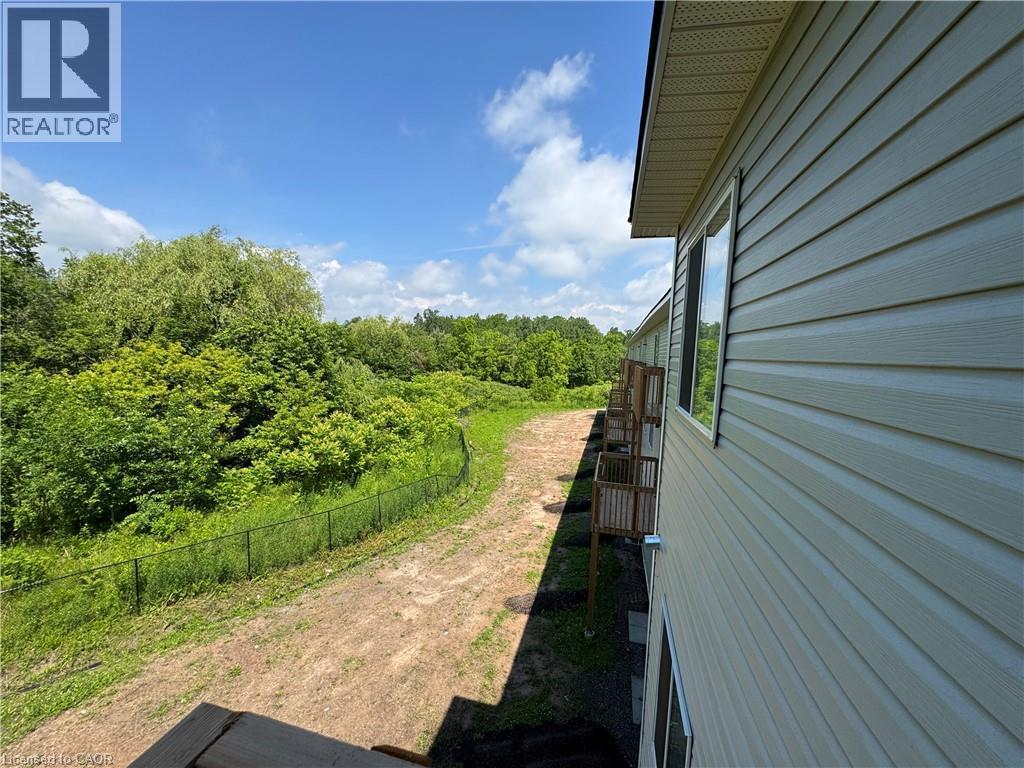 Exterior siding with multiple windows and attached balconies, bordered by a black chain-link fence and abundant greenery - 119 Highriver Trail Unit# Main, Welland, ON - Outdoor