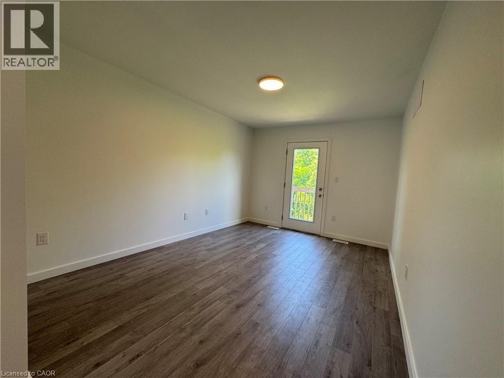 Spacious room featuring wood-finish flooring, white baseboards, and a rear door with a full-pane glass insert leading to an exterior balcony - 133 Highriver Trail Unit# Main, Welland, ON