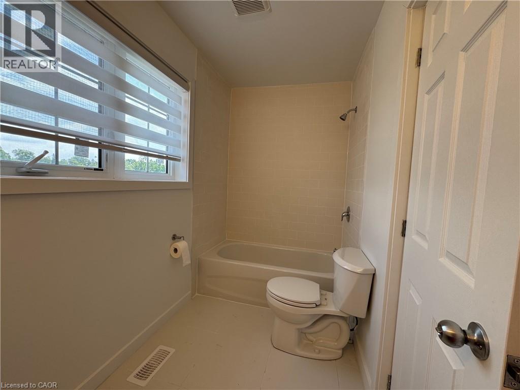 Full bathroom featuring a bathtub with shower, white toilet, and window with blinds - 133 Highriver Trail Unit# Main, Welland, ON