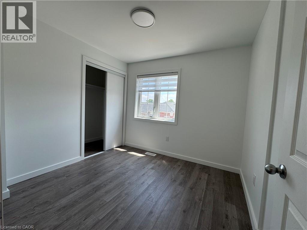 Room featuring wood-finish flooring, white baseboards, and a window with horizontal blinds - 133 Highriver Trail Unit# Main, Welland, ON