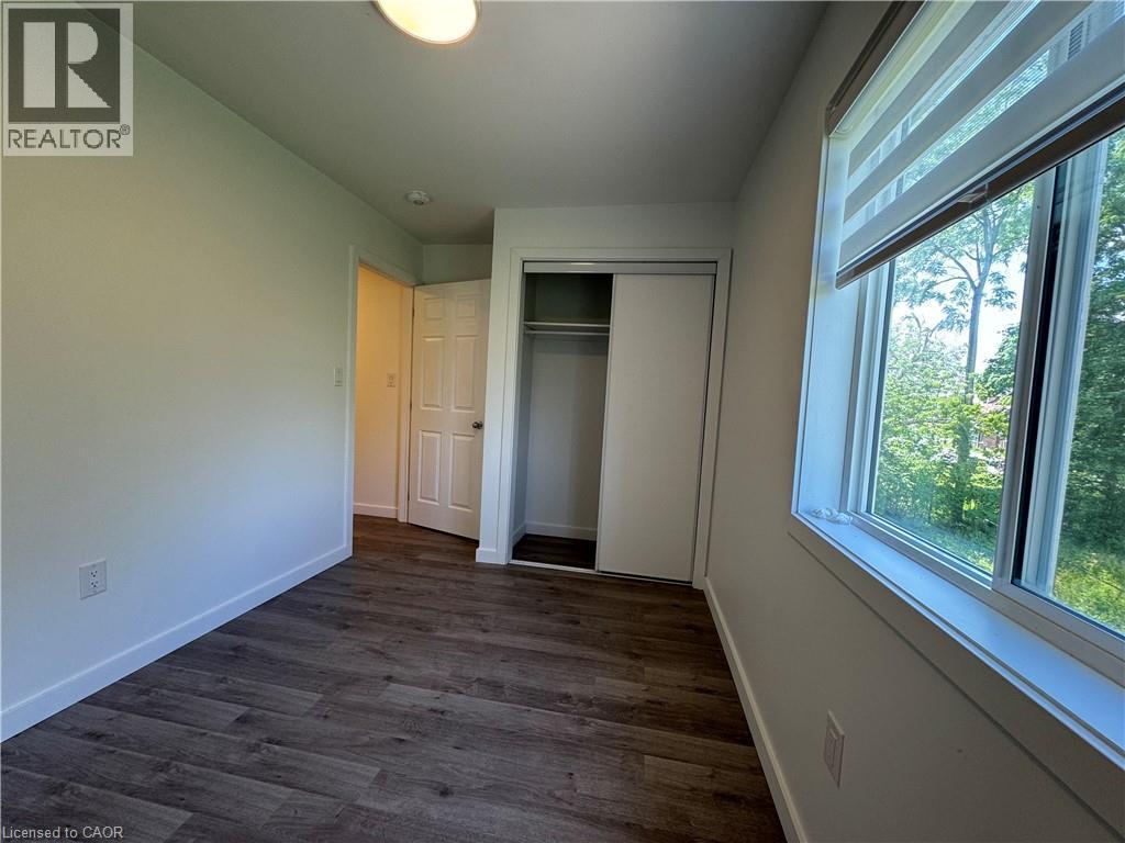 Room featuring wood-finish flooring, a double-paned window with horizontal blinds, and a built-in closet with sliding doors - 133 Highriver Trail Unit# Main, Welland, ON