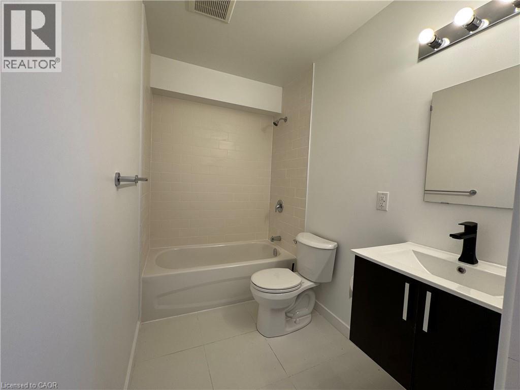 Bathroom featuring a white bathtub with subway tile surround, dark wood-finish vanity with white countertop, integrated sink, and matte black faucet, and a wall-mounted medicine cabinet - 133 Highriver Trail Unit# Main, Welland, ON