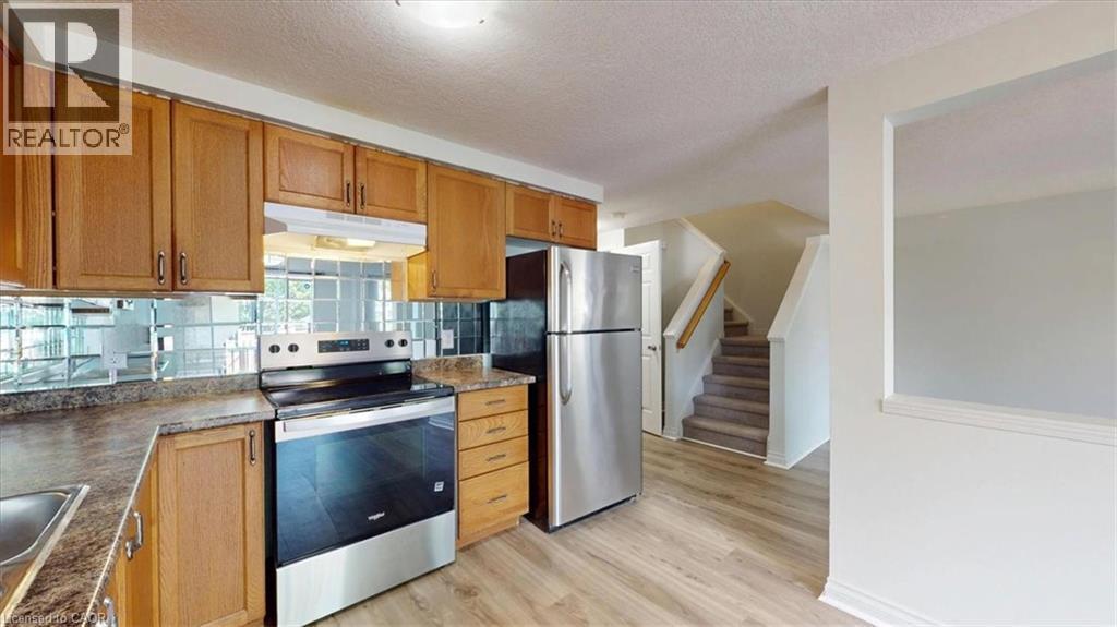 Kitchen featuring wood cabinetry, stainless steel appliances, a mirrored tile backsplash, and wood-finish flooring - 980 Creekside Drive, Waterloo, ON - Indoor Photo Showing Kitchen