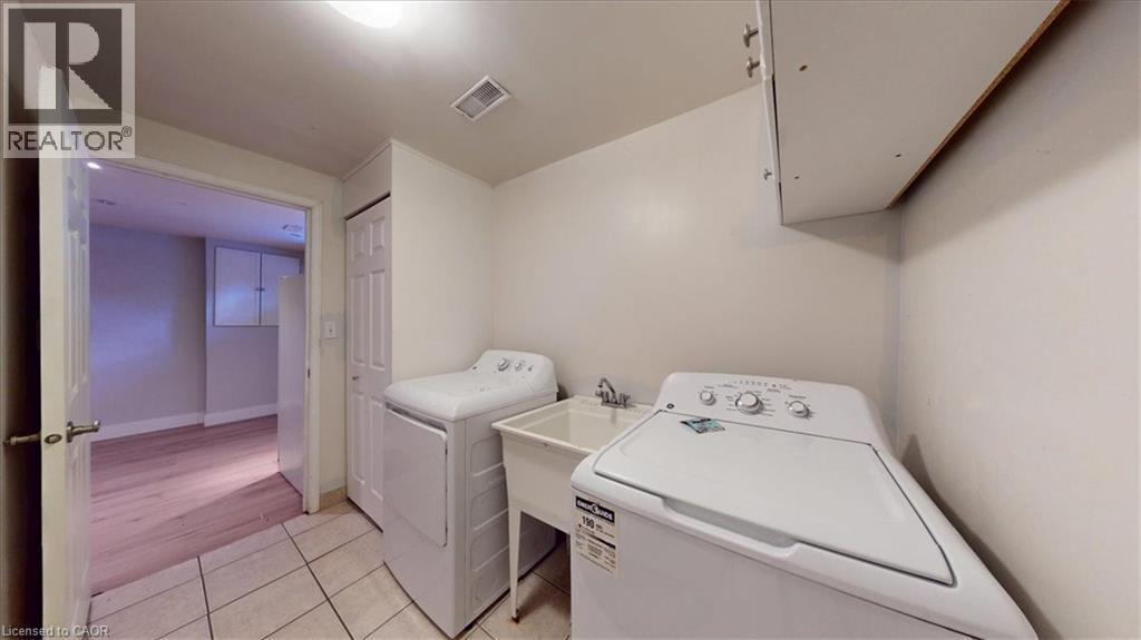 Dedicated laundry area featuring ceramic tile flooring, a utility sink with faucet, and overhead cabinetry - 980 Creekside Drive, Waterloo, ON - Indoor Photo Showing Laundry Room