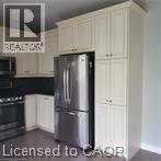 Kitchen featuring white shaker-style cabinetry, dark countertops, a built-in microwave, and a stainless steel refrigerator - 249 Bussel Crescent, Milton, ON