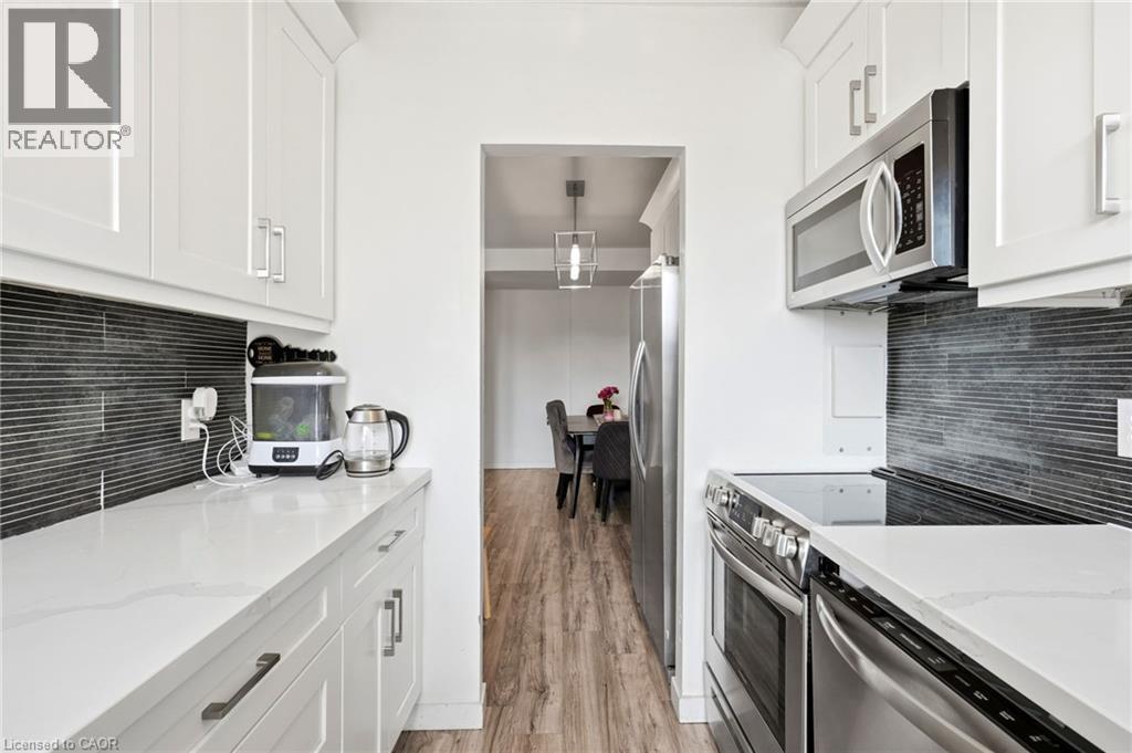 Galley kitchen featuring white cabinetry, light-toned countertops, and a dark horizontal tile backsplash - 15 Nicklaus Drive Unit# 17, Hamilton, ON