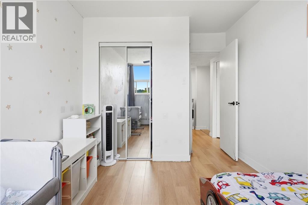 Interior room featuring wood-finish flooring, white walls, a mirrored closet door, and a white six-cube storage unit - 15 Nicklaus Drive Unit# 17, Hamilton, ON