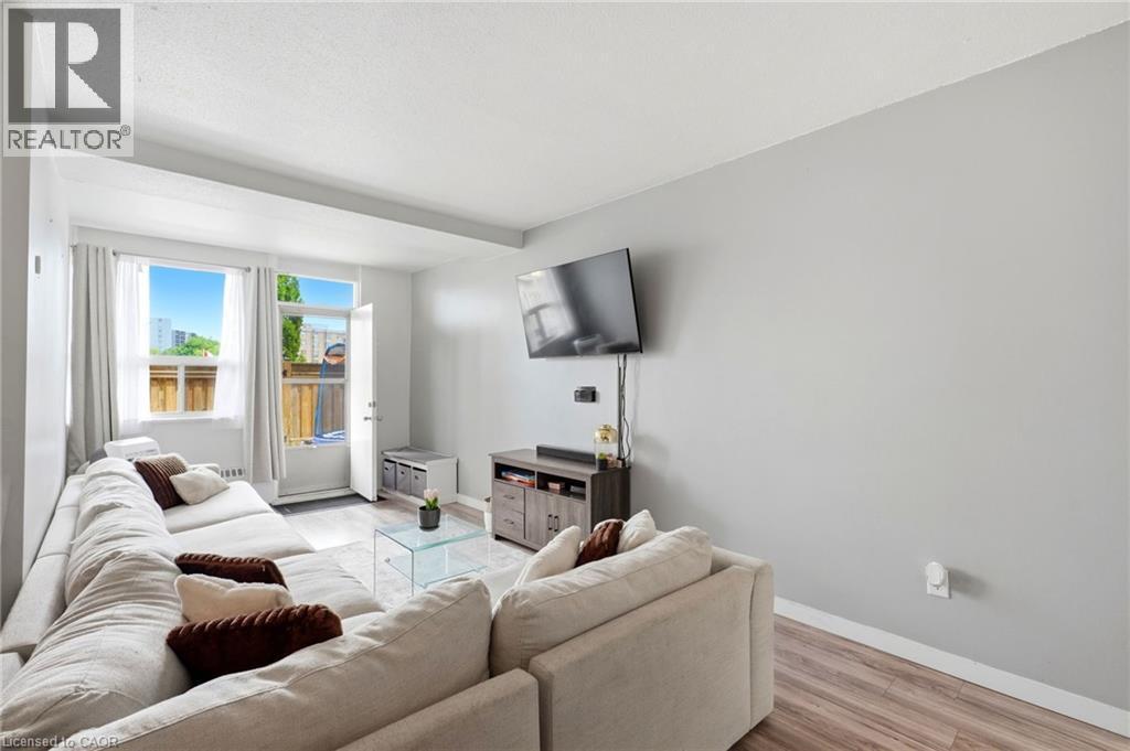Spacious living area featuring light-toned walls, wood-finish flooring, and a large window providing outdoor access - 15 Nicklaus Drive Unit# 17, Hamilton, ON
