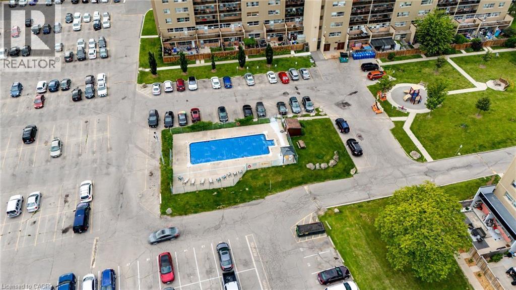 Community features include a rectangular swimming pool with surrounding concrete patio, a green space with a playground, and multiple asphalt parking areas - 15 Nicklaus Drive Unit# 17, Hamilton, ON