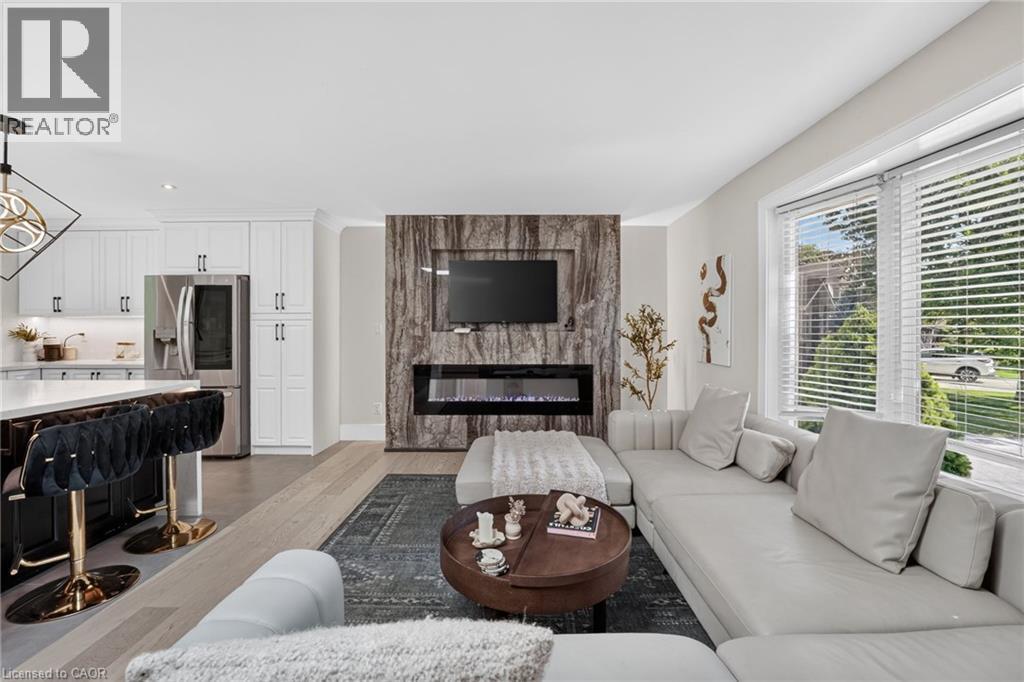 Living area featuring a floor-to-ceiling accent wall with an electric fireplace, wood-finish flooring, and large windows with horizontal blinds - 9 Leslie Drive, Hamilton, ON - Indoor Photo Showing Living Room With Fireplace