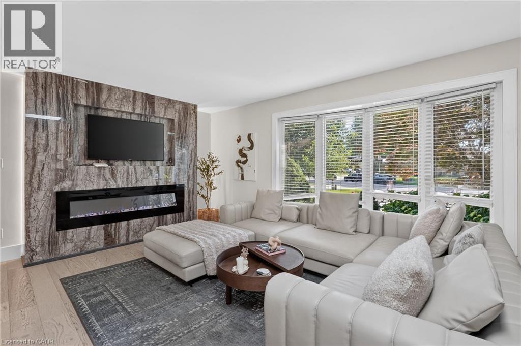 Living area featuring a modern fireplace with a linear insert set into a stone-clad wall, large multi-pane windows with blinds, and light wood-finish flooring - 9 Leslie Drive, Hamilton, ON - Indoor Photo Showing Living Room With Fireplace
