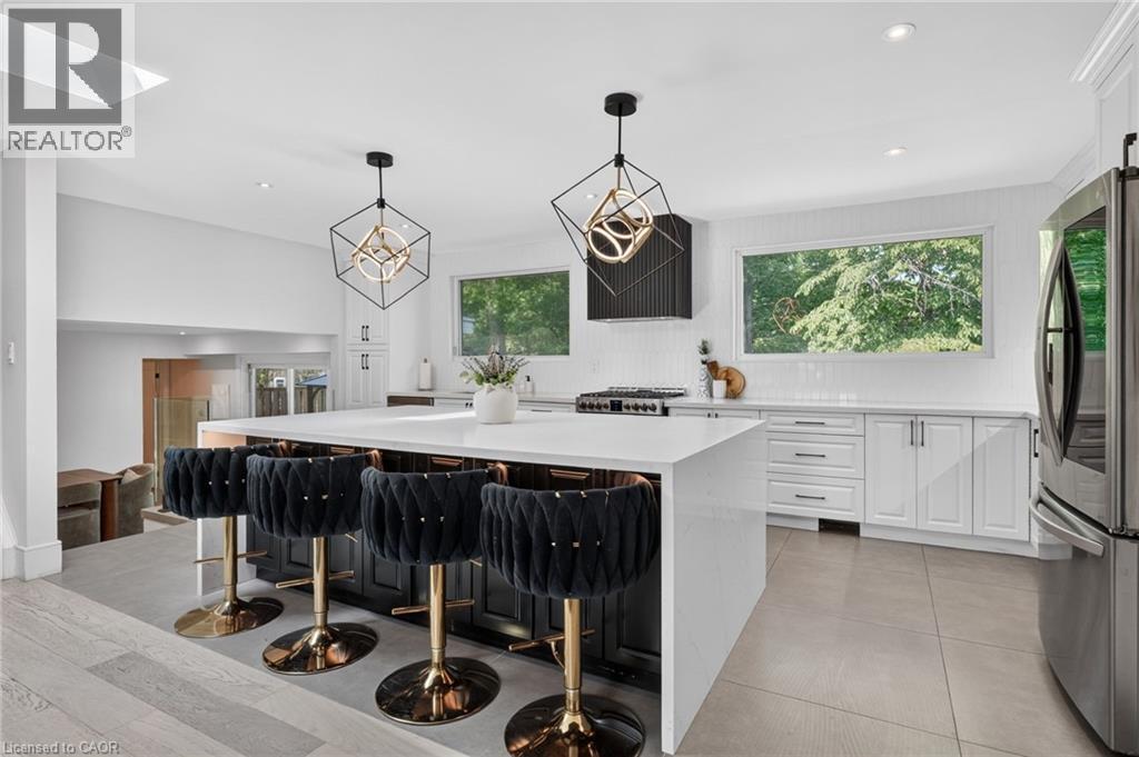 Spacious kitchen featuring a large central island with seating, pendant lighting, white cabinetry, a tiled backsplash, and stainless steel appliances - 9 Leslie Drive, Hamilton, ON - Indoor