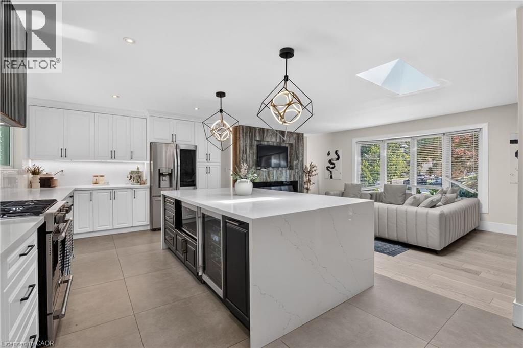 Open-concept kitchen featuring white shaker cabinetry, stainless steel appliances, a large center island with built-in beverage coolers, and sleek quartz countertops - 9 Leslie Drive, Hamilton, ON - Indoor Photo Showing Kitchen With Upgraded Kitchen