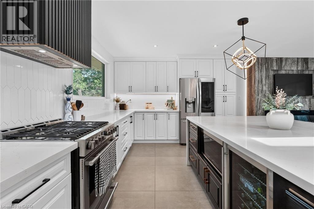 Bright kitchen featuring a black range hood, white shaker-style cabinetry, a large kitchen island with under-counter wine refrigeration, and stainless steel appliances - 9 Leslie Drive, Hamilton, ON - Indoor Photo Showing Kitchen With Upgraded Kitchen