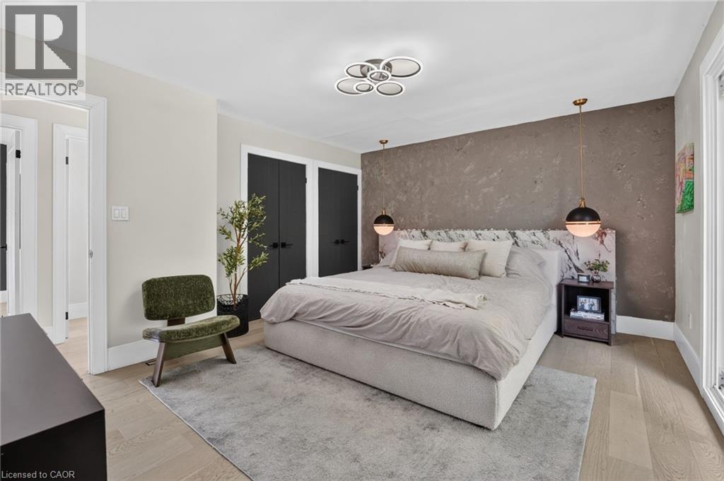 Bedroom featuring light wood-finish flooring, a textured accent wall, dual black wardrobe doors, and a modern ceiling fixture - 9 Leslie Drive, Hamilton, ON - Indoor Photo Showing Bedroom