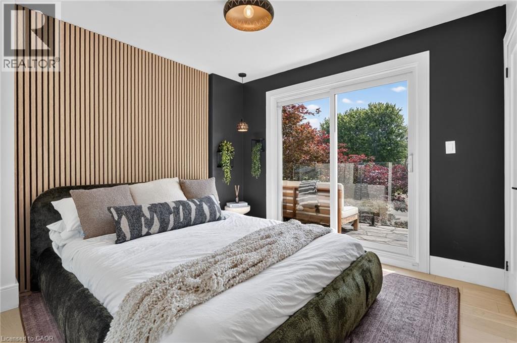 Bedroom with a slatted wood accent wall, light wood-finish flooring, and a sliding glass door leading to a stone patio - 9 Leslie Drive, Hamilton, ON - Indoor Photo Showing Bedroom