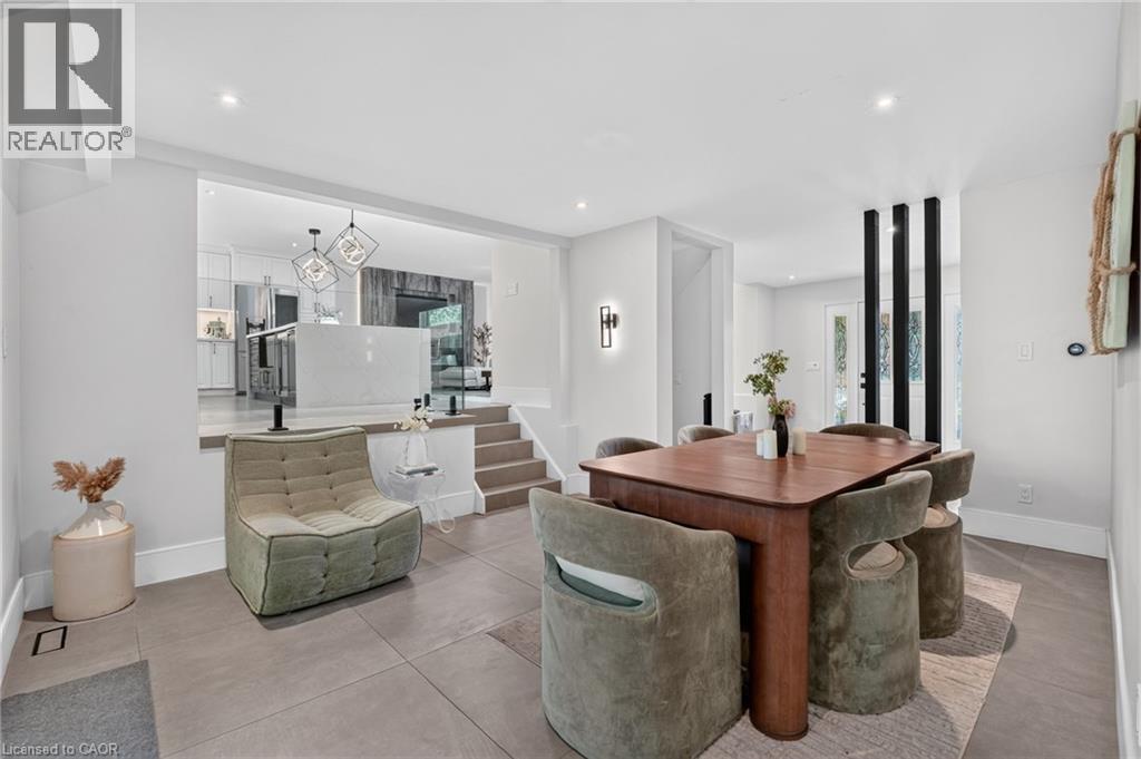 Multi-level interior featuring a wood dining table, recessed lighting, wall sconce, and a kitchen with an island and geometric pendant lights visible through a wide opening - 9 Leslie Drive, Hamilton, ON - Indoor