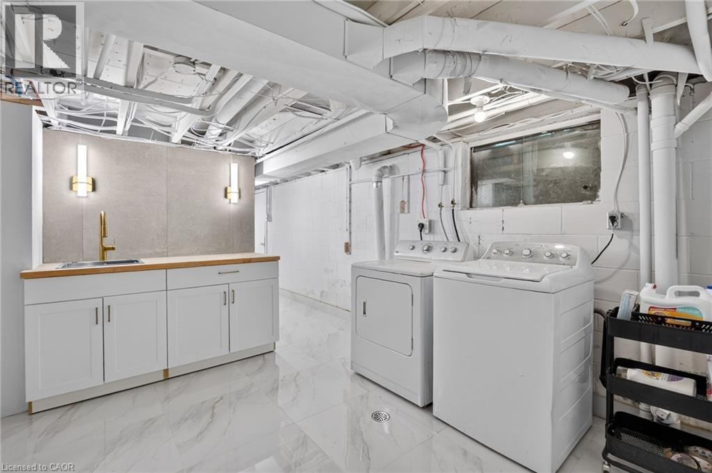 Laundry area featuring white appliances, a wood-finish countertop, a built-in sink with a gold-finish faucet, and a stone-look backsplash - 9 Leslie Drive, Hamilton, ON - Indoor Photo Showing Laundry Room