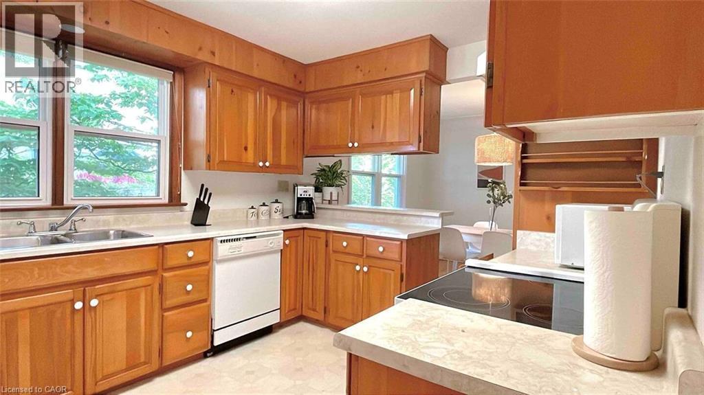 Kitchen featuring wood cabinetry, light-toned countertops, a stainless steel double-basin sink, and a white dishwasher - 919 Montgomery Drive, Ancaster, ON