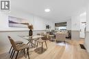 Open-concept living area featuring light wood-finish flooring, white and light grey wainscoting, a large front window, recessed lighting, and a white entry door with a frosted glass pane - 11 Ford Street, Hamilton, ON 
