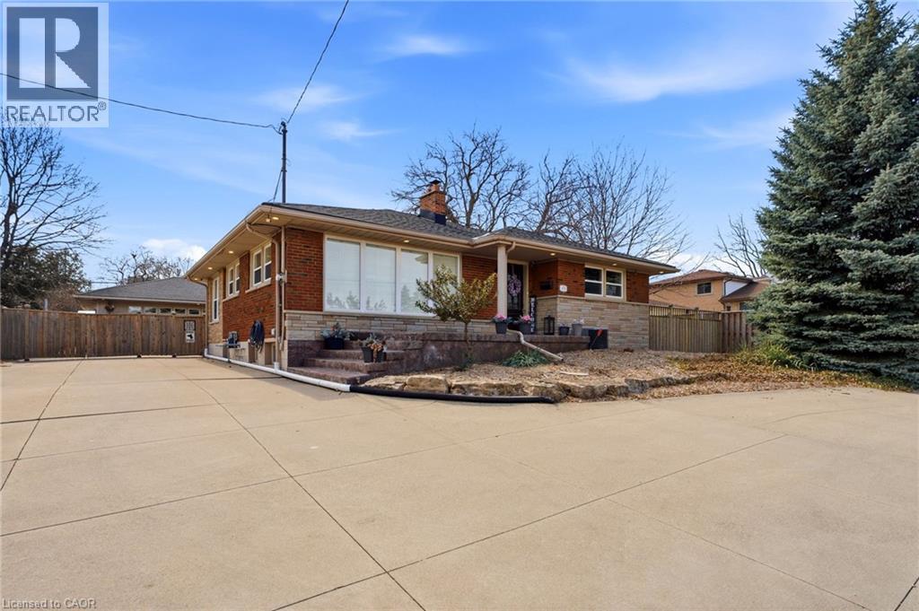 View of front facade featuring a chimney, stone siding, brick siding, and driveway - 473 Mohawk Road W, Hamilton, ON