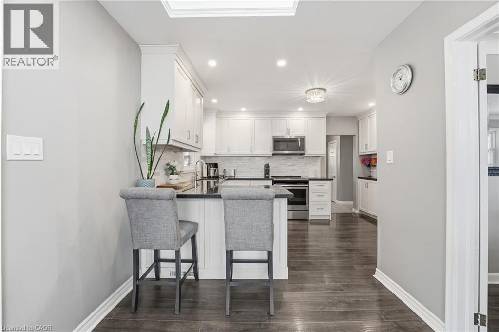 Kitchen featuring white cabinets, stainless steel appliances, dark wood finished floors, recessed lighting, and a peninsula - 473 Mohawk Road W, Hamilton, ON