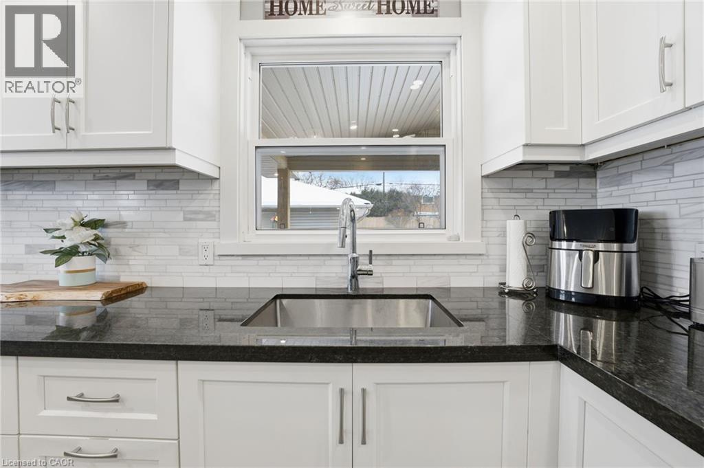 Kitchen with white cabinets, dark stone counters, and backsplash - 473 Mohawk Road W, Hamilton, ON