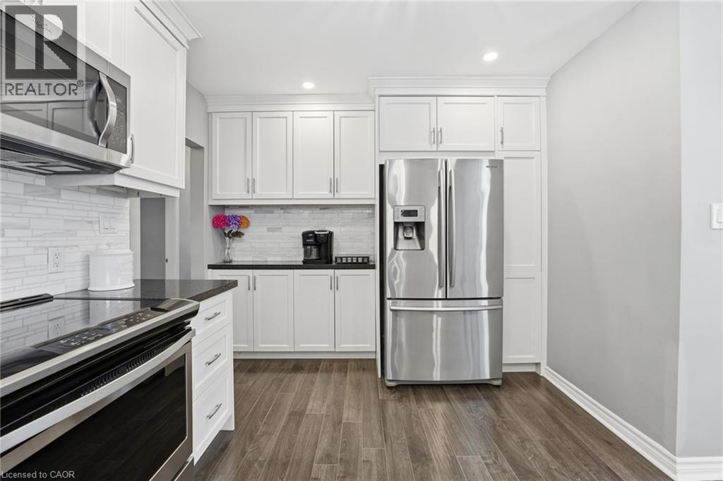 Kitchen featuring stainless steel appliances, white cabinetry, dark wood finished floors, recessed lighting, and backsplash - 473 Mohawk Road W, Hamilton, ON