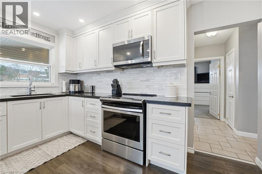 Kitchen with stainless steel appliances, white cabinets, and dark wood-style flooring - 473 Mohawk Road W, Hamilton, ON