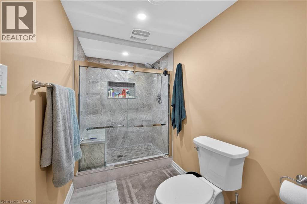 Glass-enclosed shower with gray stone-finish wall tile, a built-in bench, and an integrated niche - 149 Kinsman Drive, Binbrook, ON