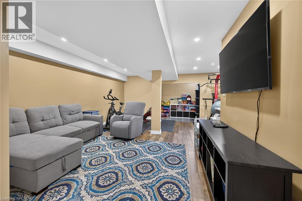 Recessed lighting illuminates the space, featuring wood-finish flooring and a built-in media console - 149 Kinsman Drive, Binbrook, ON