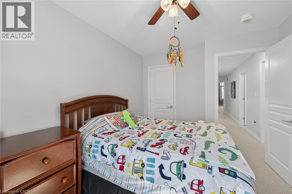 Light gray painted walls define this bedroom with a wood-finish bed frame, wood-finish ceiling fan with integrated lighting, and light-colored carpeting - 149 Kinsman Drive, Binbrook, ON